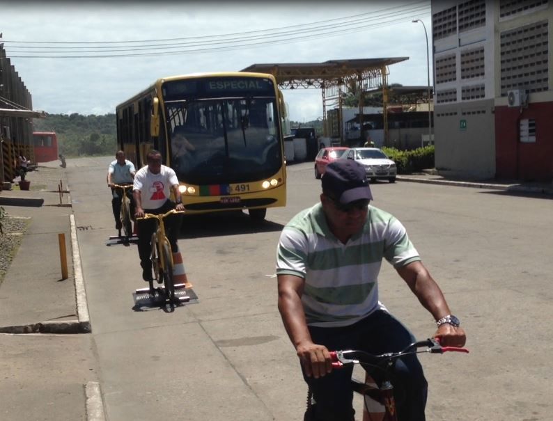 Ciclistas pedalam em bicicletas fixas na via enquanto ônibus passam próximos, em ação do Projeto Amigo Môto